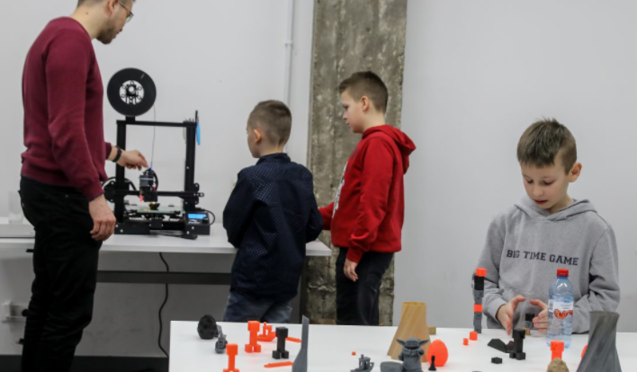Dzieci wraz z prowadzącym warsztaty przy drukarce 3D.